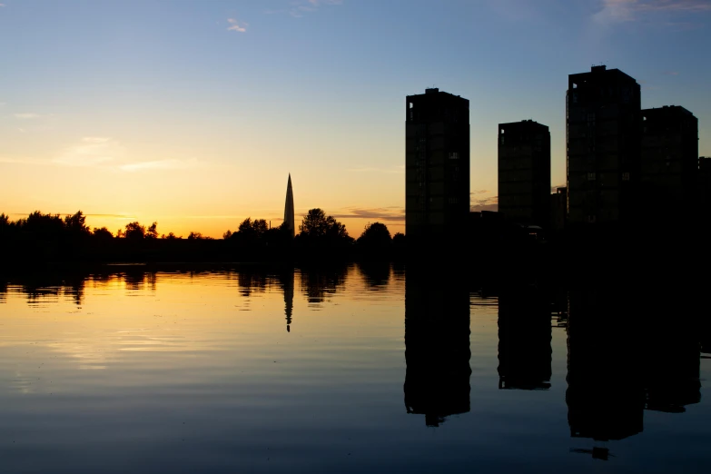 a body of water with tall buildings in the background, an album cover, by Washington Allston, unsplash, coventry city centre, nuclear sunset, view from the lake, three towers