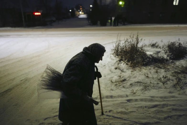 a man riding skis down a snow covered street, by Attila Meszlenyi, blessing the soil at night, documentary photograph, an elderly, sweeping