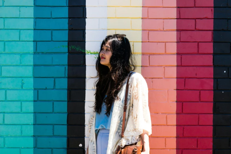 a woman standing in front of a colorful wall, by Whitney Sherman, pexels contest winner, color field, asian girl with long hair, painted on a brick wall, white hue, hippie chic