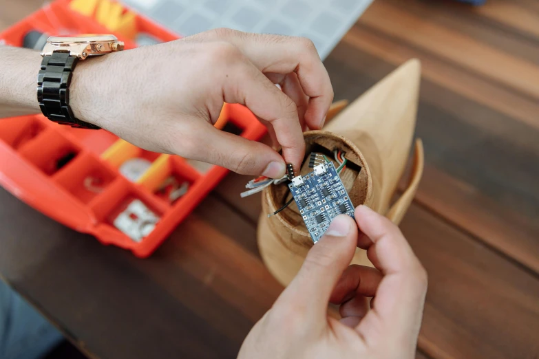 a close up of a person holding a cell phone, a cross stitch, cone shaped, spaceship being repaired, on a wooden tray, arduino