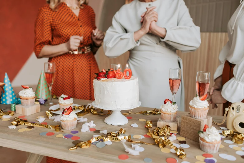 a group of people standing around a table with a cake, by Julia Pishtar, pexels contest winner, orange and white color scheme, pals have a birthday party, red white and gold color scheme, pair of keycards on table