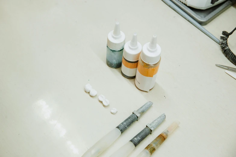 three tubes of ink and three bottles of paint sitting on top of a counter