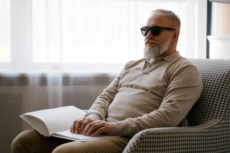 a man sitting in a chair reading a book, an album cover, inspired by John E. Berninger, unsplash, hyperrealism, implanted sunglasses, white beard, middle - age, at home