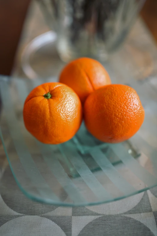 three oranges sitting on a glass plate on a table