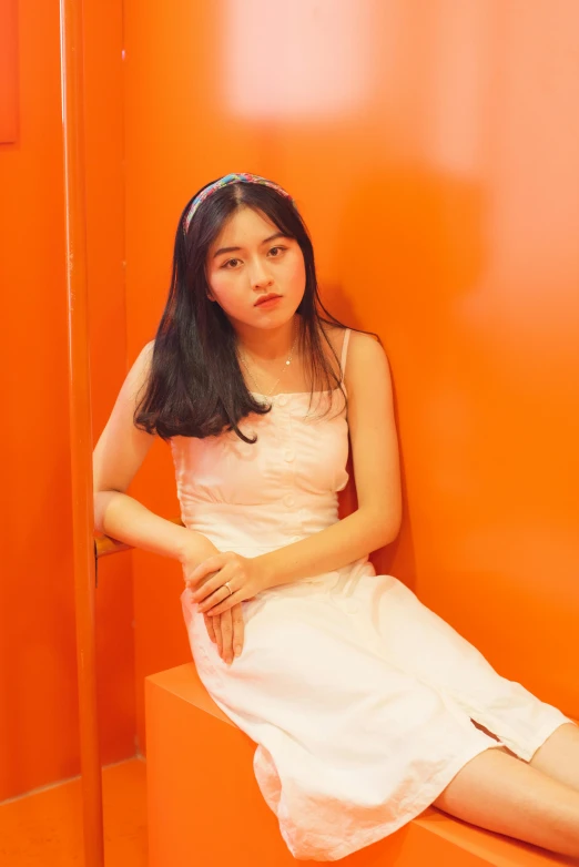 a woman sitting on a bench in front of an orange wall, an album cover, inspired by Kim Jeong-hui, instagram, realism, wearing a cute white dress, 🤤 girl portrait, ulzzang, non blurry