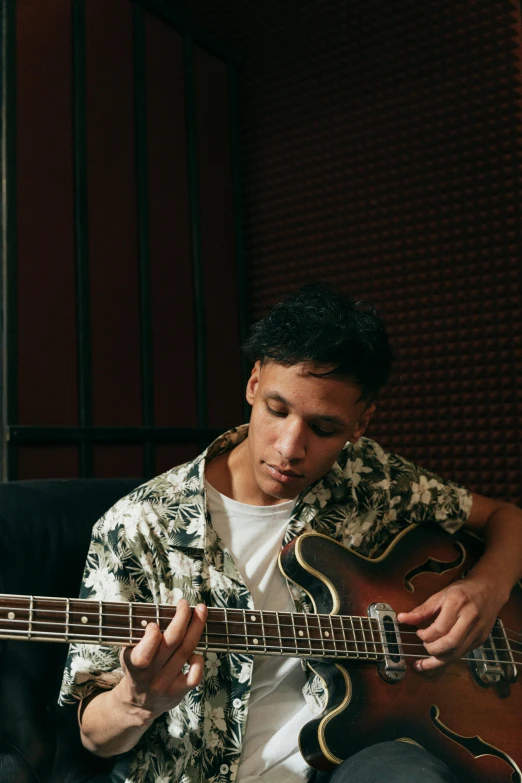 a man sitting on a couch playing a guitar, an album cover, by Alejandro Obregón, pexels contest winner, bassist, slightly tanned, profile pic, alexis franklin