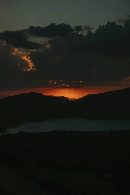 a lake surrounded by hills with the sun setting