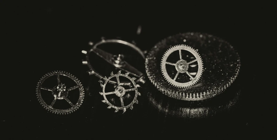 a close up of a clock on a table, a black and white photo, by Adam Marczyński, pexels contest winner, kinetic art, cogs and springs and jewels, on black paper, miniature product photo, high detailed wheels