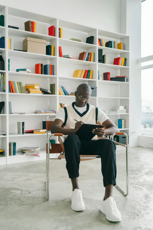 a man sitting in a chair reading a book, inspired by David Bailly, pexels contest winner, adut akech, in a open-space working space, lance reddick, snapchat photo