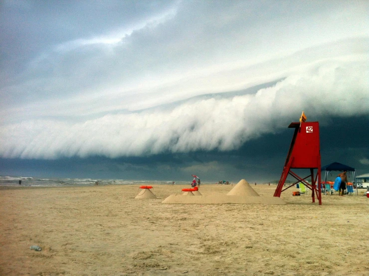 a red lifeguard tower sitting on top of a sandy beach, a photo, inspired by Storm Thorgerson, massive clouds, green smoggy sky, imgur, towering cumulonimbus clouds