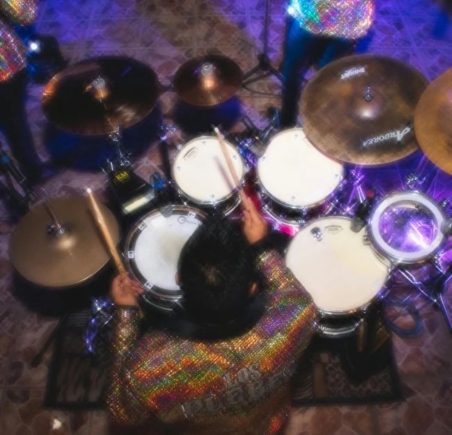 a man sitting in front of a drum set, pexels contest winner, birdseye view, holographic tones, live performance, vivid rich colors