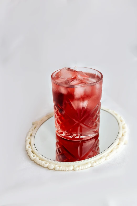 a red drink sitting in a glass on a plate