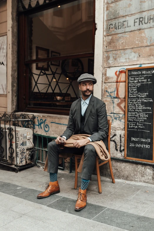 a man sitting on a bench in front of a building, dapper, sitting in a cafe, simone graci, tweed colour scheme