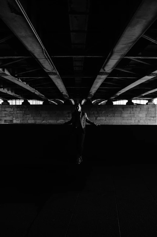 black and white pograph of person standing under a bridge