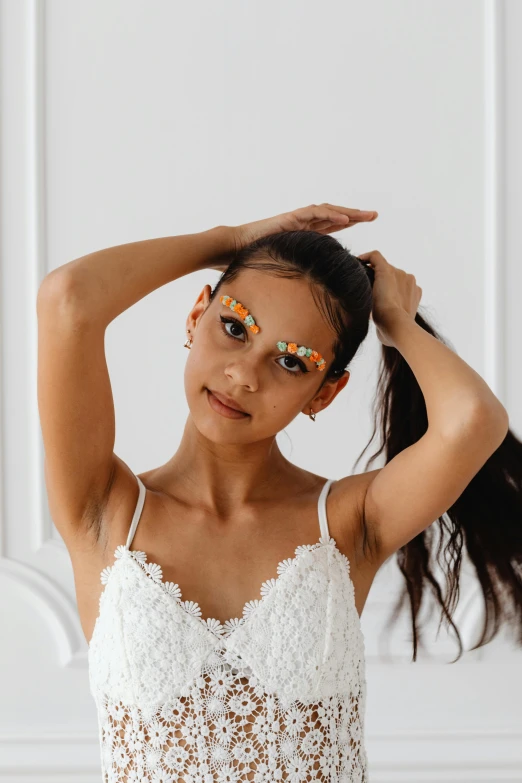 a woman standing in front of a white wall, by Julia Pishtar, trending on pexels, toyism, posing in leotard and tiara, orange pupils, young teen, floral patterned skin