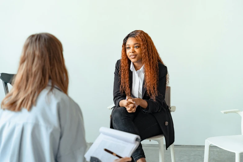 a woman sitting in a chair talking to another woman, trending on pexels, black, schools, on a gray background, clinical