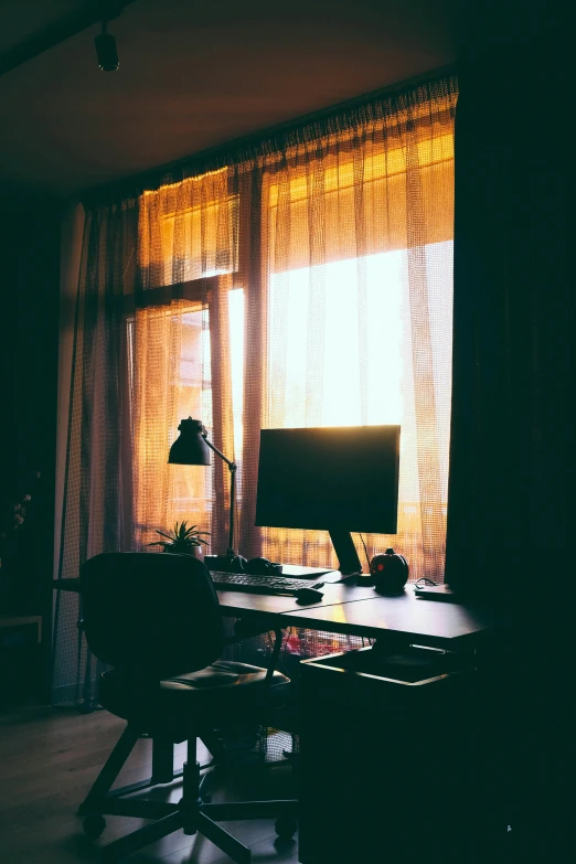 sunlight streams in through curtains to a desk with a computer on it