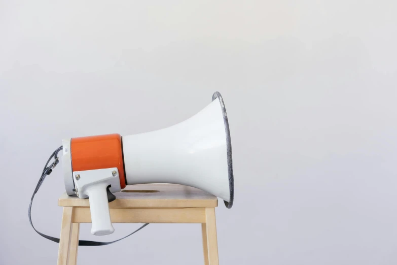 a white and orange megaphone sitting on top of a wooden stand, trending on unsplash, hyperrealism, background image, front left speaker, grey, hyperrealism photo