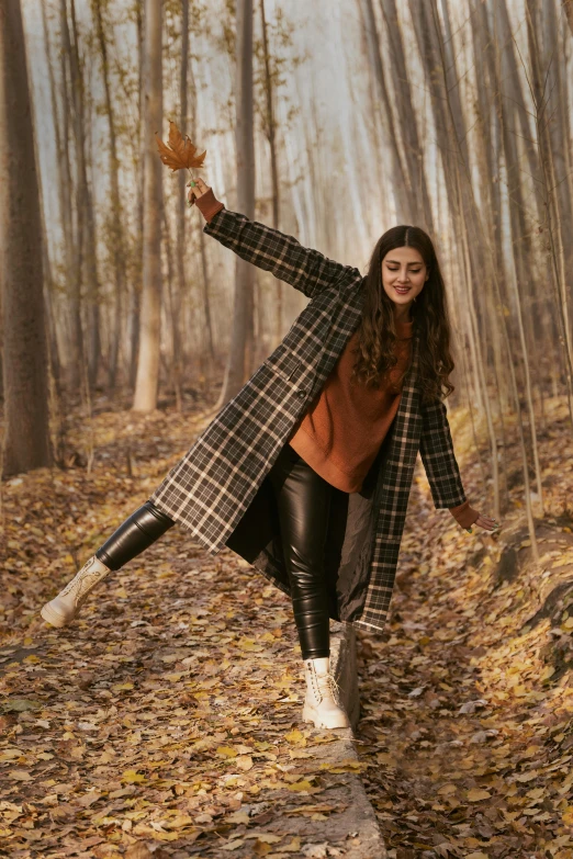 a woman is walking down a path in the woods, trending on pexels, arabesque, doing a sassy pose, flannel, wearing a long coat, leaves in the air