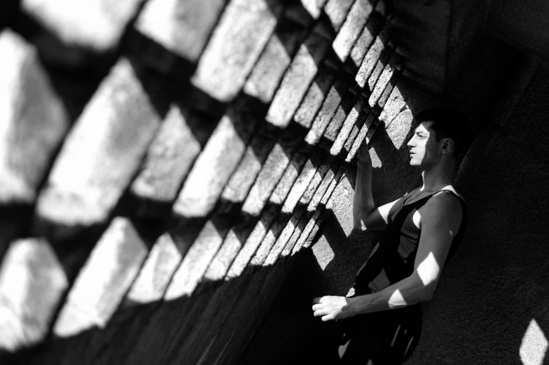 a black and white photo of a man leaning against a wall, inspired by Max Dupain, unsplash, conceptual art, with fractal sunlight, bricks, yoga, female looking