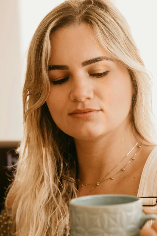 a woman sitting at a table with a cup of coffee, an album cover, inspired by Louisa Matthíasdóttir, trending on pexels, beautiful face detail, wearing gold detailed choker, eyes closed, blonde