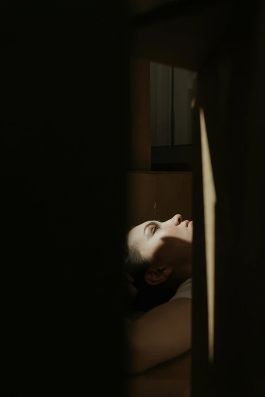 a woman laying on a bed in a dark room, her face is in shadow, looking through a window frame, promo image, ignant