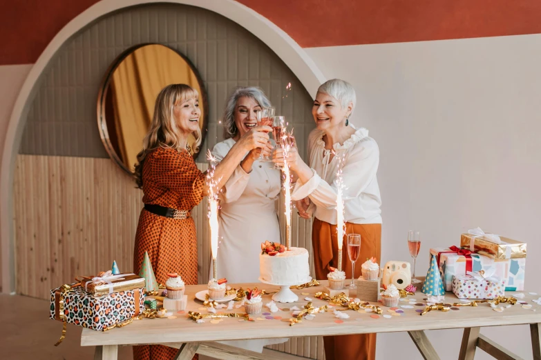 a group of women standing around a table with a cake, by Liza Donnelly, pexels contest winner, light red and orange mood, bubbly, white background, three