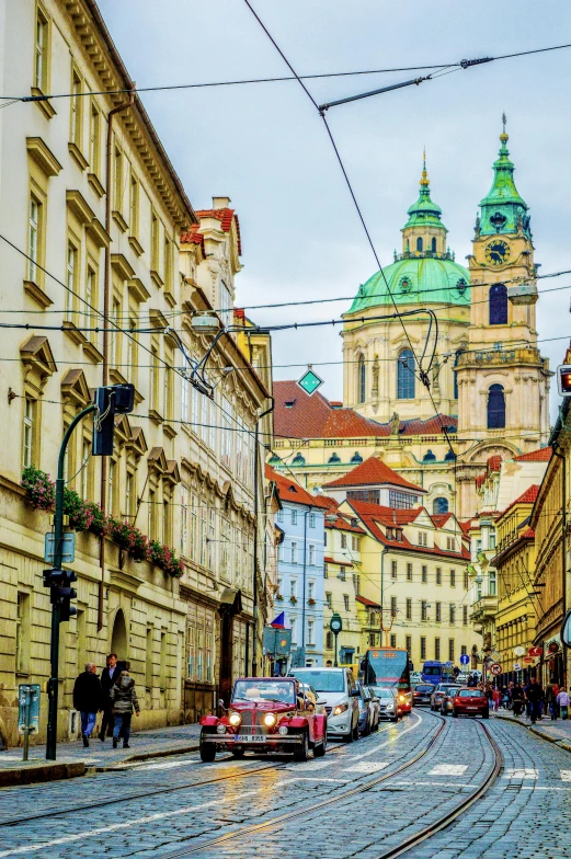 a street filled with lots of traffic next to tall buildings, by Antoni Brodowski, pexels contest winner, art nouveau, church in the background, prague, wires hanging above street, street of teal stone