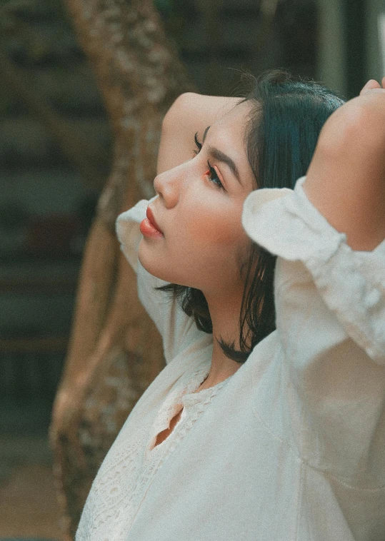 a woman in a white shirt standing next to a tree, inspired by Elsa Bleda, trending on pexels, visual art, young cute wan asian face, cream colored peasant shirt, concert, looking her shoulder