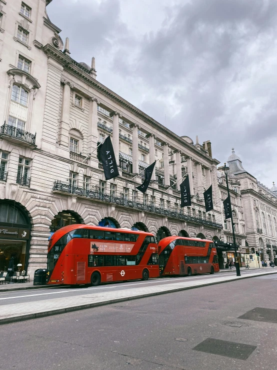 two red double decker busses are parked on the side of the street