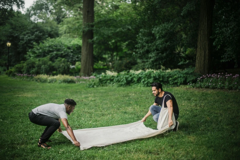 a couple of men standing next to each other on top of a lush green field, an album cover, by Daniel Gelon, pexels contest winner, process art, people on a picnic, long flowing fabric, crawling on the ground, central park