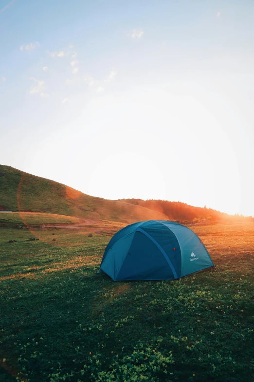 a blue tent sitting on top of a lush green field, setting sun, adventure gear, hillside, profile pic