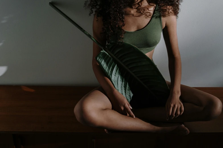 a beautiful young woman sitting on top of a wooden table, inspired by Elsa Bleda, trending on pexels, renaissance, big leaf bra, olive thigh skin, in a bedroom, green clothing