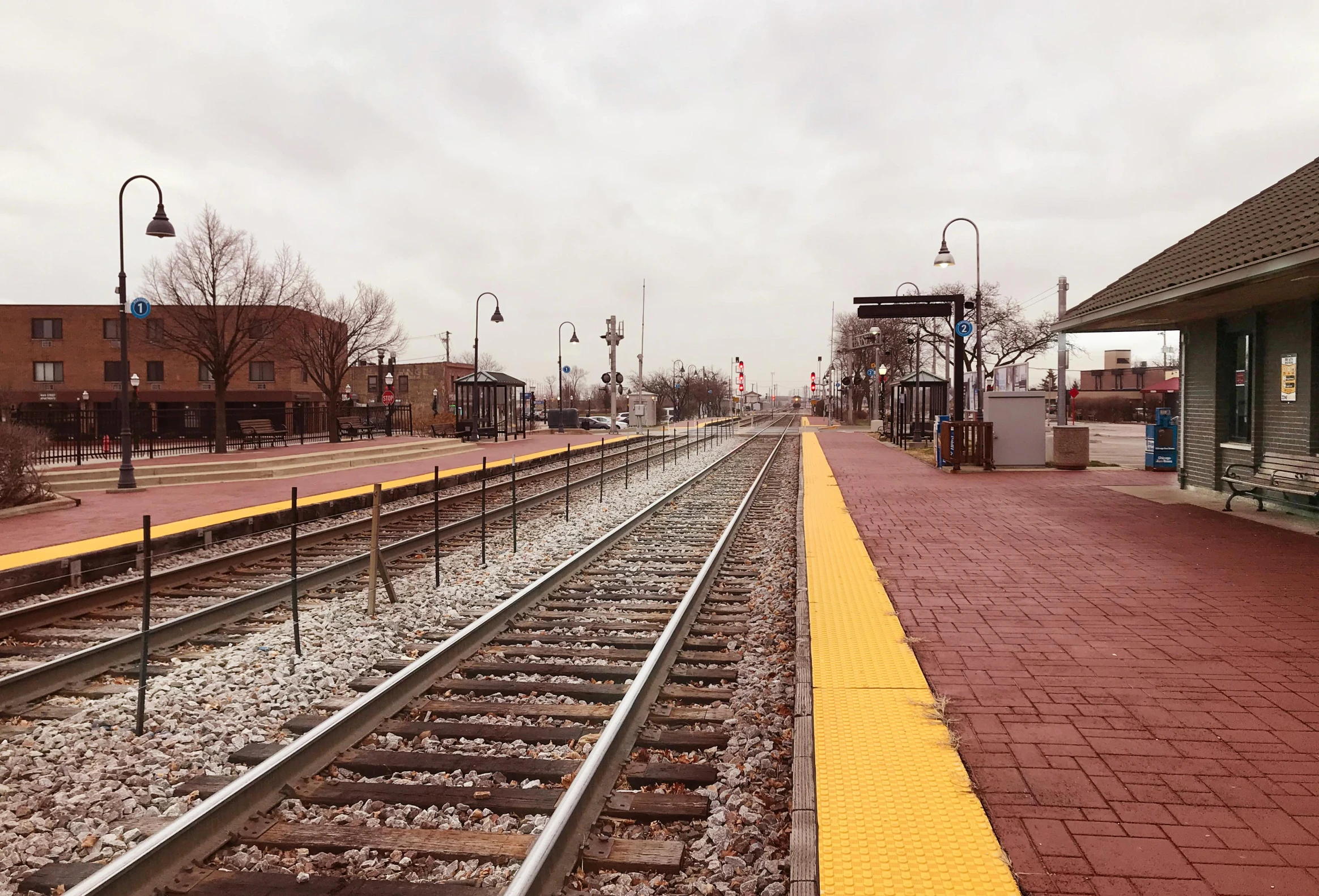 a train station with a train on the tracks, by Carey Morris, empty streetscapes, from wheaton illinois, slight overcast weather, square