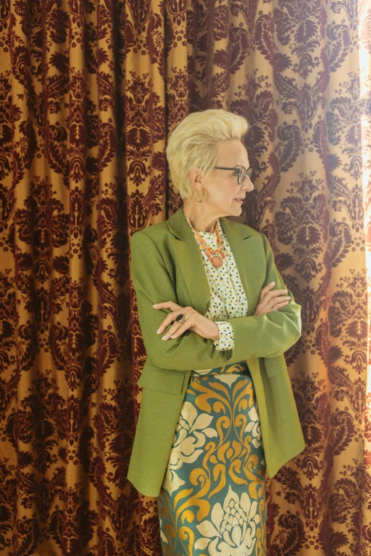 a woman standing in front of a curtain, an album cover, inspired by Elizabeth Charleston, rococo, wearing a suit and glasses, green and brown clothes, gillian anderson, filmstill