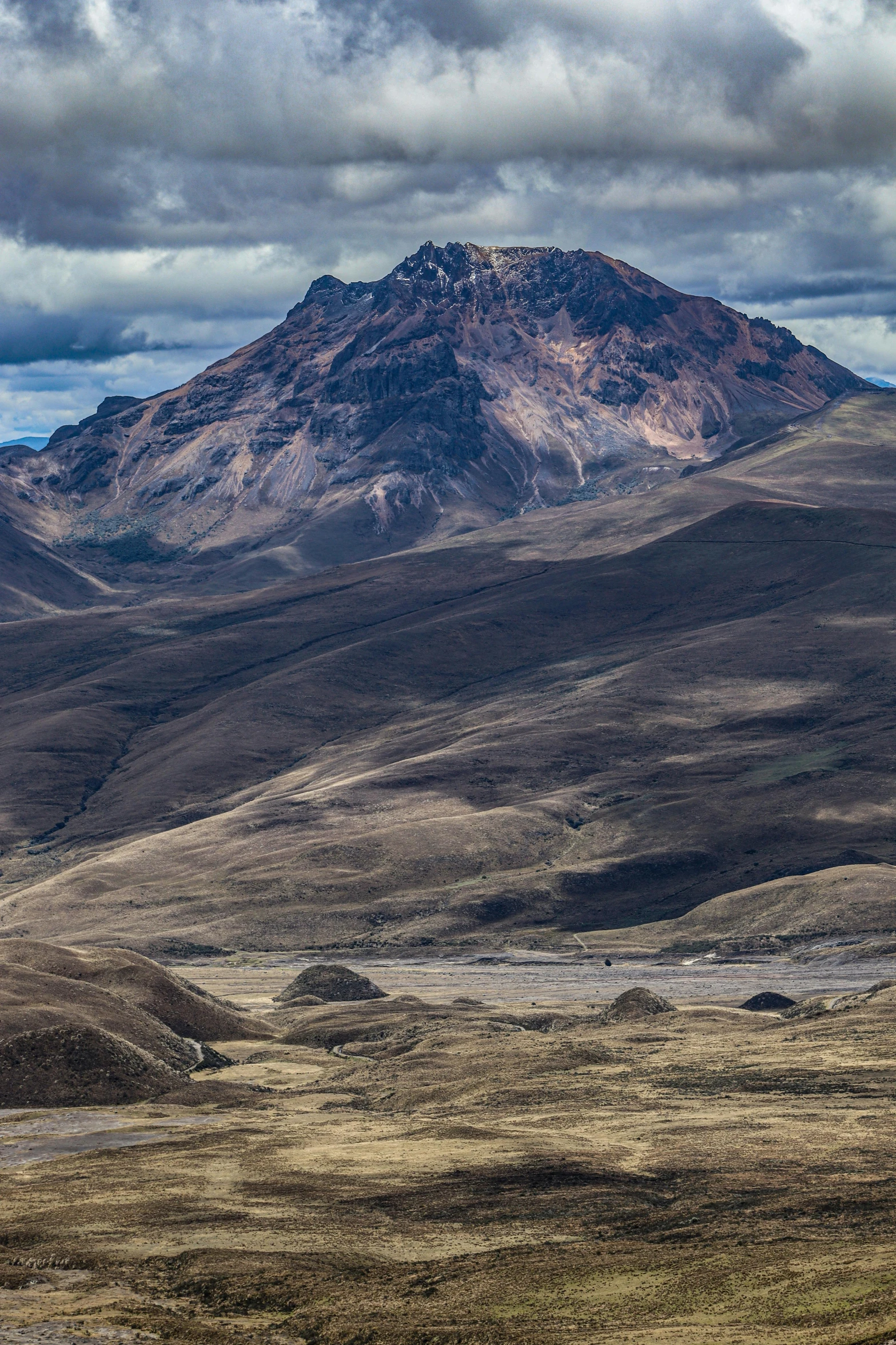 a big mountain range with some brown grass and dirt