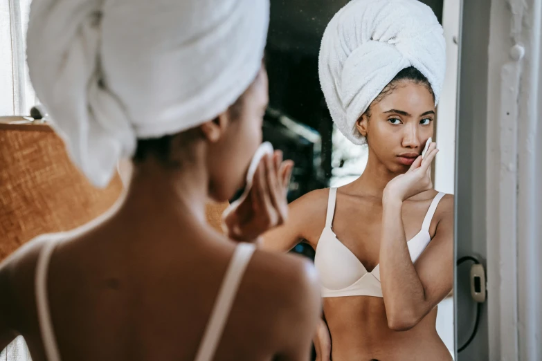 a woman standing in front of a mirror with a towel on her head, trending on pexels, renaissance, brown skinned, disrobed, tan skin), early evening