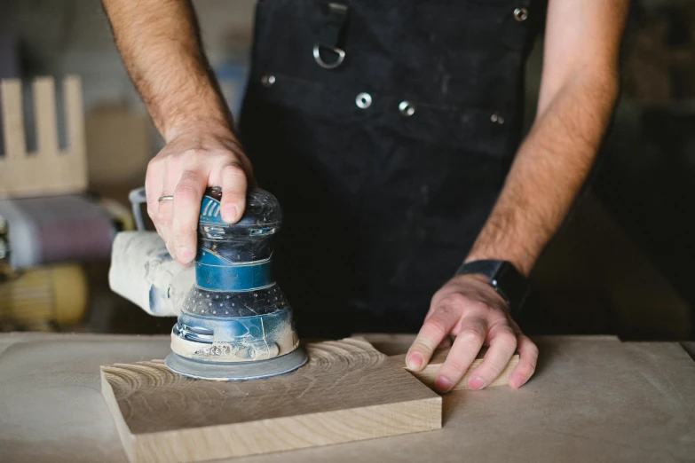 a man sanding a piece of wood with a sander, a portrait, pexels contest winner, blue print, wearing an apron, james collinson, sleek hands