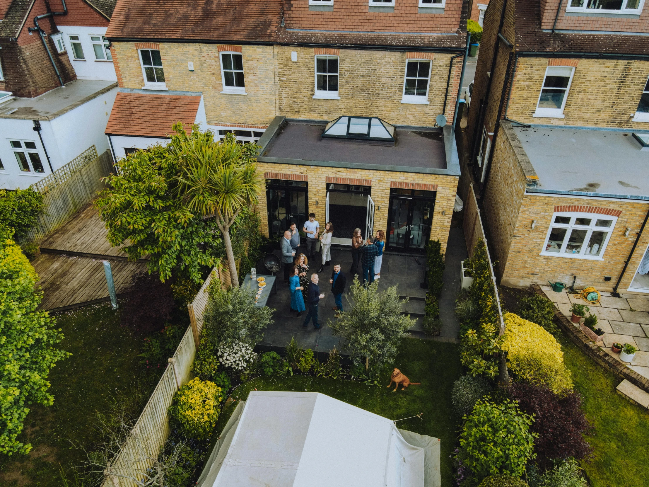 a group of people standing outside of a house, unsplash, private press, wide aerial shot, esher, roof garden, fully covered