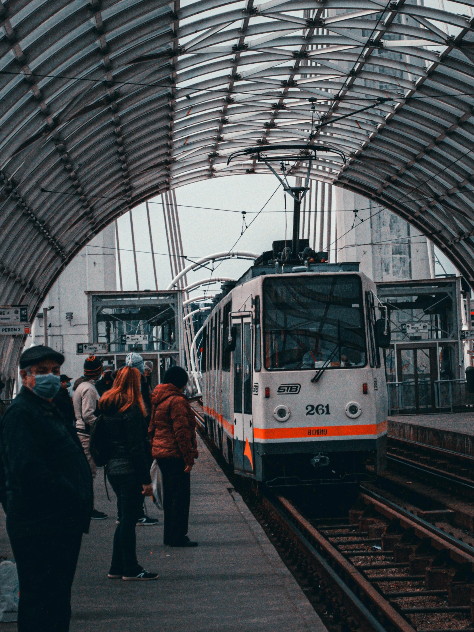 a group of people waiting for a train at a train station, by Adam Marczyński, pexels contest winner, street tram, 🚿🗝📝, a cathedral under an overpass, grey