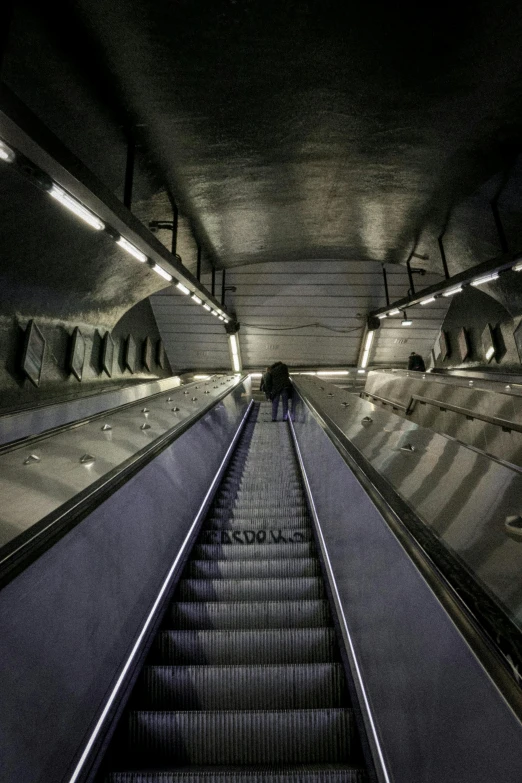 an escalator going down the middle of a tunnel, inspired by Alfred Eisenstaedt, unsplash, stockholm, under light, station, madrid