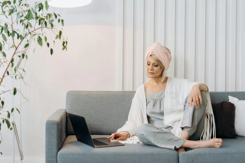 a woman sitting on a couch with a laptop, trending on pexels, turban, gandalf as a woman, white and pink cloth, knees upturned