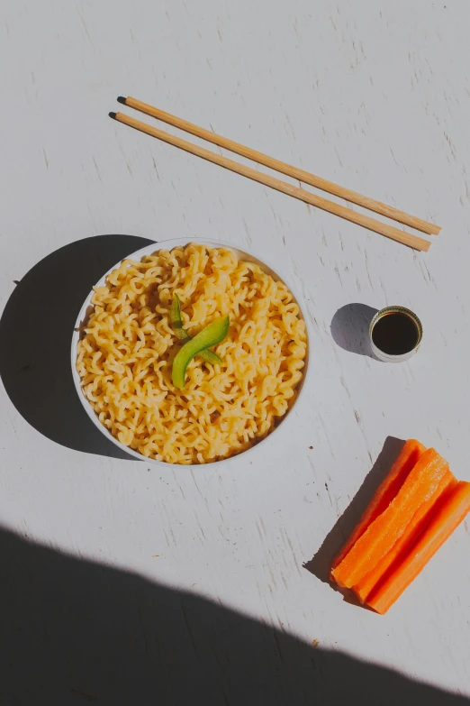 a bowl of noodles, carrots, and chopsticks on a table, detailed product image, detail shot, sun drenched, vanilla