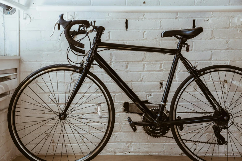 a black bicycle leaning against a white brick wall, pexels contest winner, on a wooden desk, profile image, mechanics, tournament