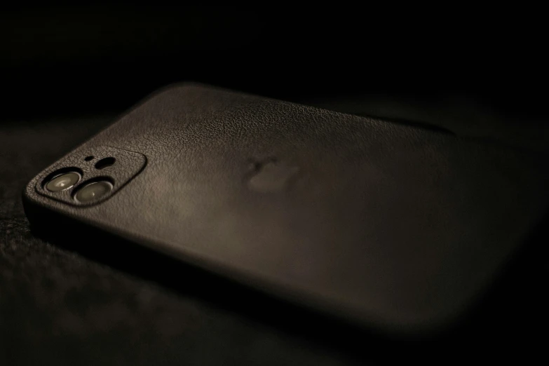 a close up of a cell phone on a table, by Niels Lergaard, unsplash, photorealism, black leather, iphone 12, stealth, dark-skinned