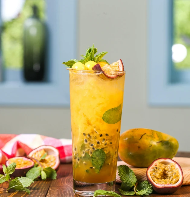 a glass filled with fruit sitting on top of a wooden table, passion fruits, mint, fan favorite, greens)