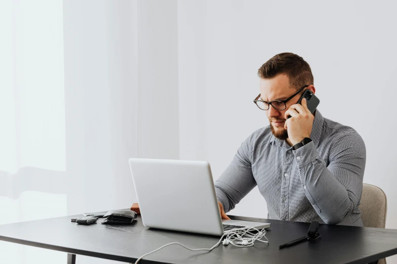 a man sitting at a desk talking on a cell phone, trending on pexels, laptops, worksafe. instagram photo, lachlan bailey, man with glasses