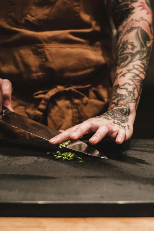 the tattooed person is using a knife to cut some greens