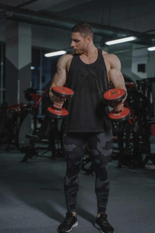 a shirtless man standing in a gym with three orange dumbbells