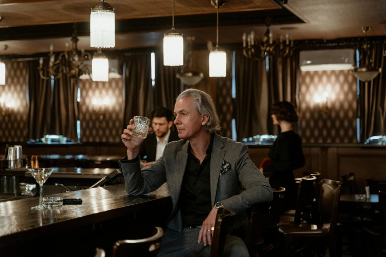 a man sitting at a bar holding a glass of wine, a portrait, by Emma Andijewska, pexels contest winner, a silver haired mad, mid-twenties, drinking whiskey, promotional image